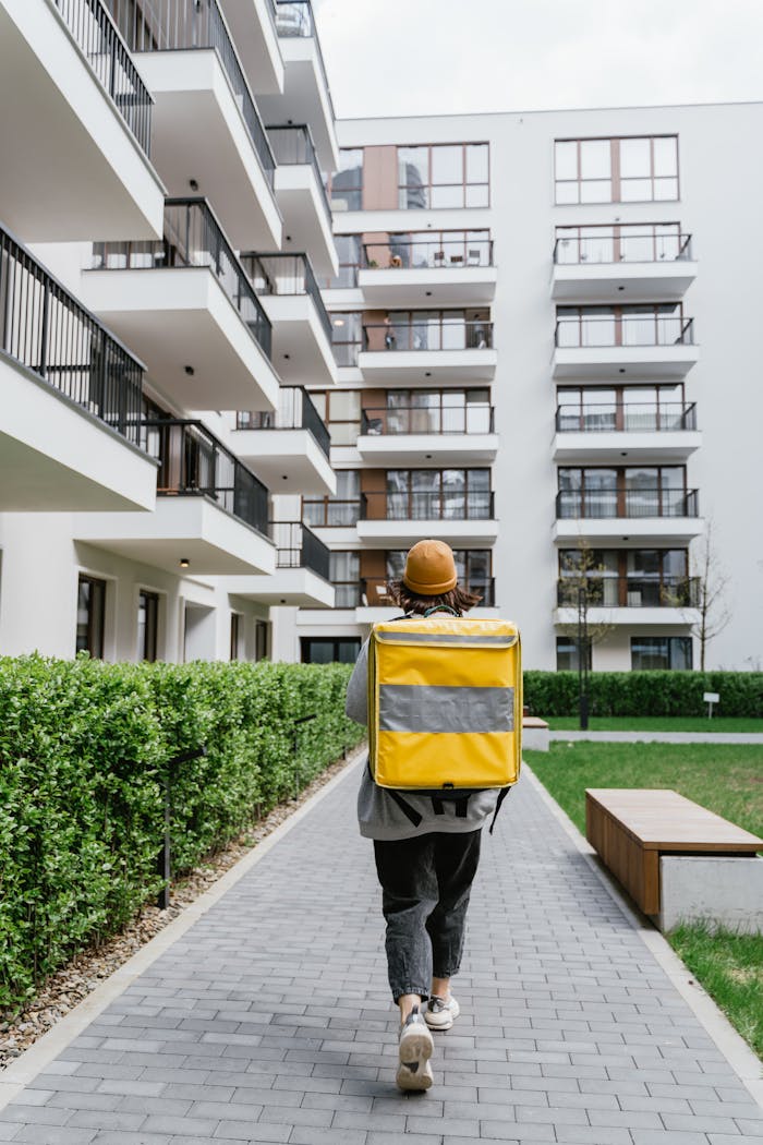 Courier with a yellow thermal bag delivering in a modern apartment complex.